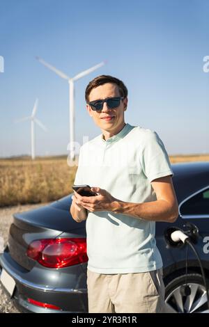 Homme avec voiture électrique de charge. Éoliennes en arrière-plan. Banque D'Images