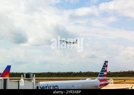 Avion d'American Airlines décollant de la piste sous ciel couvert, capturé près du terminal avec des avions stationnés. Cancun. Mexique. Banque D'Images