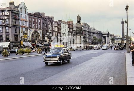 Photo histricale d'un taxi, des bus et de la circulation sur O'Connell Street avec la statue de Daniel O''Connell (le libérateur), Dublin, Irlande dans les années 1960 Banque D'Images