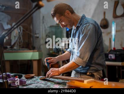 Luthier professionnel axé sur la réparation détaillée de guitare dans un environnement d'atelier authentique. Artisan montrant son expertise et son dévouement dans le mu traditionnel Banque D'Images