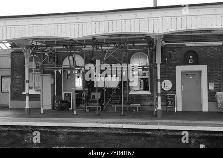 Emsworth, Hampshire, Angleterre. 26 août 2024. Vue en niveaux de gris d'une partie de la gare d'Emsworth soutenue par un échafaudage, avec un café et des bagages vintage exposés. Banque D'Images