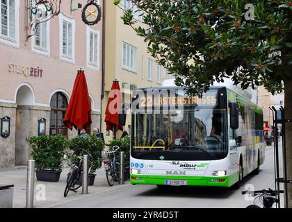 Salzbourg, Autriche - 1er octobre 2024 : City bus à Salzbourg, Autriche, passant devant les cafés de rue et les bâtiments historiques avec des parasols rouges et un parking à vélos Banque D'Images