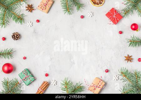 Cadre de Noël fait de branches de sapin, décorations rouges, boîtes-cadeaux, nourriture de Noël et pommes de pin sur fond de béton gris. Pose à plat. Bonne année Banque D'Images