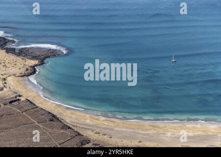 Vue sur la plage avec mer ondulée, côte sablonneuse et voilier solitaire à l'horizon, îles Canaries, Lanzarote, Espagne, Europe Banque D'Images
