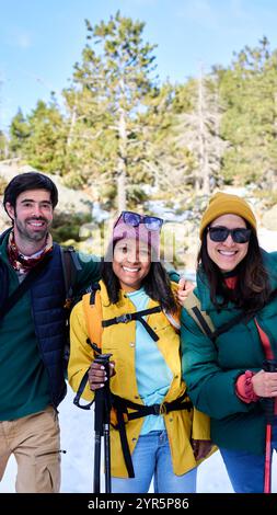 Portrait joyeux de trois amis multirraciaux randonnant dans une forêt enneigée pendant les vacances d'hiver. Banque D'Images