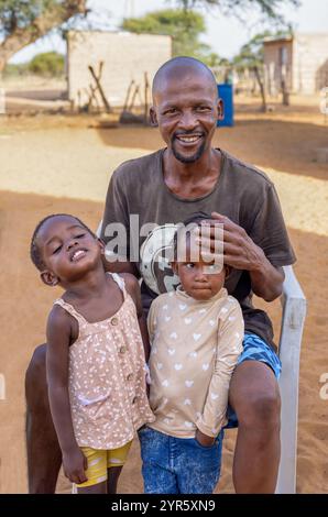 village famille africaine, portrait heureux père jouant avec deux enfants filles avec des tresses, assis sur une chaise dans la cour Banque D'Images