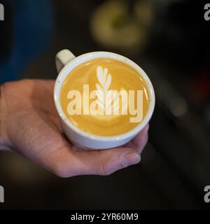 Barista tenant un Latte fraîchement préparé avec Leaf Latte Art Banque D'Images