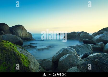 Longue exposition des vagues brumeuses de la mer s'écrasant sur les roches moussues au coucher du soleil créant une atmosphère sereine magique, vila nova de gaia, porto Banque D'Images