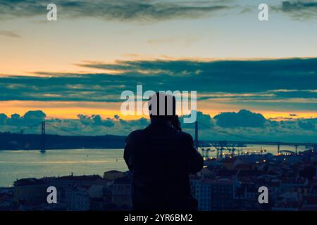Silhouette d'un photographe prenant des photos du magnifique coucher de soleil sur lisbonne, portugal, mettant en vedette l'emblématique pont 25 de abril et le paysage urbain Banque D'Images