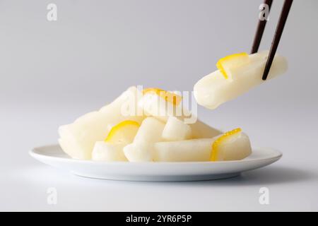 Image de radis marinés au vinaigre doux et à la saveur de yuzu (fond blanc) soulevée avec des baguettes Banque D'Images