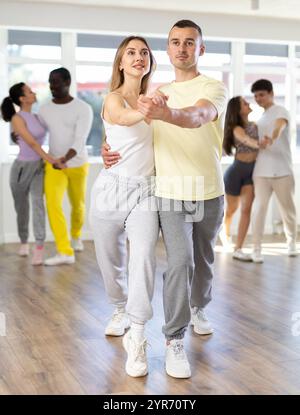 Heureux homme caucasien et fille dans les vêtements de sport dansant cha-cha-cha danse dans le studio de danse pendant la classe de groupe Banque D'Images