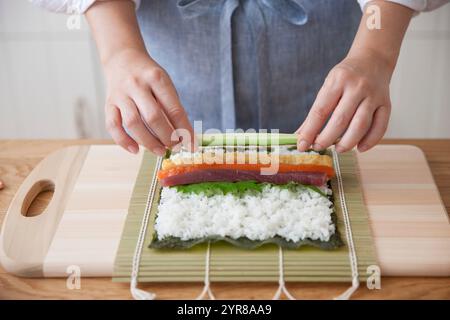 Femme fabriquant des rouleaux de sushi avec du riz vinaigre et des ingrédients sur la portière Banque D'Images