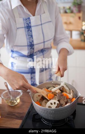 Femme faisant frire du poulet et des légumes dans une casserole Banque D'Images