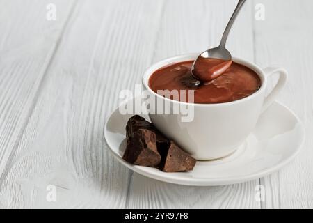 chocolat chaud dans la tasse et à la cuillère sur la table en bois blanc Banque D'Images