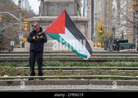 Un homme plus âgé portant des gants agite le drapeau palestinien. Des centaines de manifestants pro-palestiniens se rassemblent à Columbus Circle pour la "Journée internationale de solidarité pour le peuple palestinien" à New York. Banque D'Images