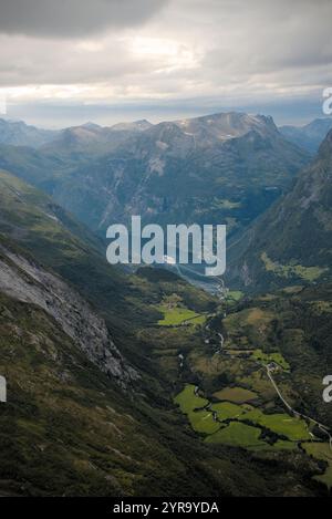 Une vue panoramique d'une perspective élevée à un bateau de croisière lointain quittant le port dans le village de Geiranger par le Geirangerfjord en Norvège Banque D'Images