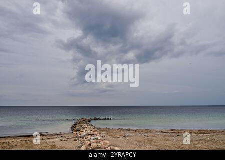 Vue depuis la plage de la mer Baltique dans des conditions météorologiques nuageuses avec un énorme nuage dramatique suspendu dans le ciel au-dessus d'un groyne de pierre (centre) Banque D'Images