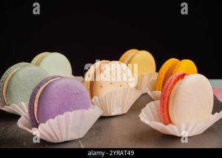 Macarons multicolores magnifiquement conçus sur un fond noir. Une merveilleuse présentation de pâtisseries exquises et de bonbons d'origine française. Banque D'Images