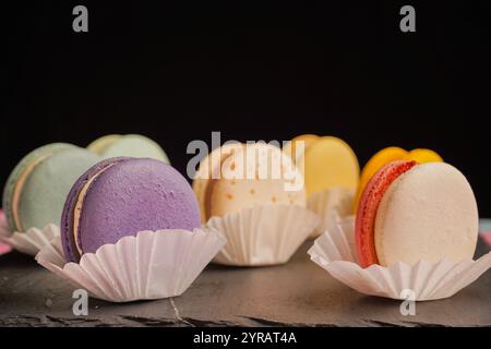 Macarons multicolores magnifiquement conçus sur un fond noir. Une merveilleuse présentation de pâtisseries exquises et de bonbons d'origine française. Banque D'Images