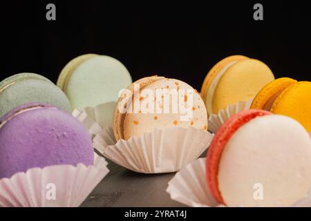 Macarons multicolores magnifiquement conçus sur un fond noir. Une merveilleuse présentation de pâtisseries exquises et de bonbons d'origine française. Banque D'Images