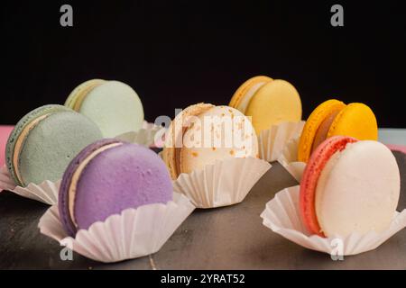 Macarons multicolores magnifiquement conçus sur un fond noir. Une merveilleuse présentation de pâtisseries exquises et de bonbons d'origine française. Banque D'Images