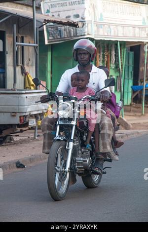 Père et enfants conduisant une moto dans une rue africaine urbaine au Togo, capturant la vie quotidienne, le regroupement familial et la culture des transports locaux Banque D'Images
