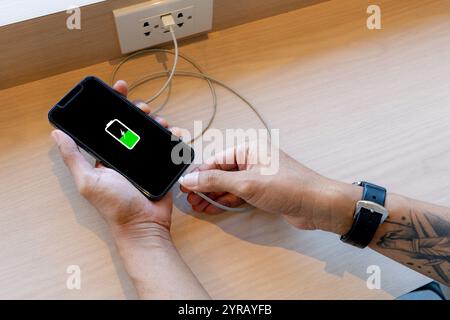 main tenant le téléphone intelligent se connectant à l'alimentation électrique pour la recharge Banque D'Images
