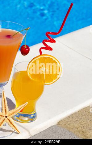 Orange fraîche avec une cerise rouge et une orange à l'intérieur sur un verre, sur fond d'une piscine bleue. Un jour ensoleillé d'été. Banque D'Images