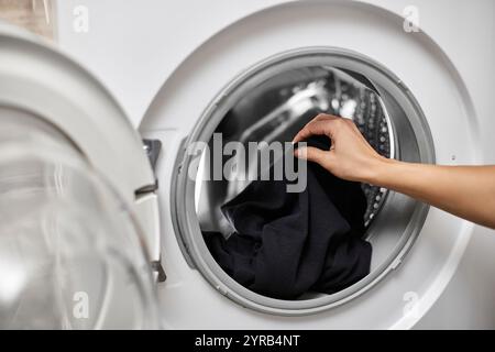 Femme mettant des vêtements en coton noir dans la machine à laver, gros plan Banque D'Images