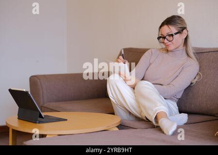 Une femme en lunettes travaillant à distance sur le canapé Banque D'Images