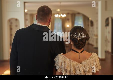 Vue arrière d'une dame et d'un monsieur habillés en tenue habillée entrant dans la salle de bal dans un intérieur classique à éclairage doux, espace photocopie Banque D'Images