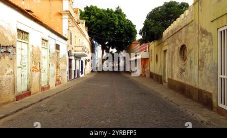 Une rue sereine du Cap-Vert avec des bâtiments colorés altérés par les intempéries et un pavé, reflétant la riche culture et le patrimoine dynamique de l'île. Banque D'Images