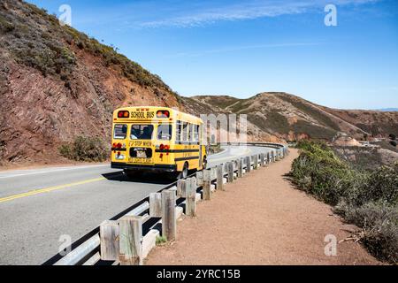 Un autobus scolaire jaune voyageant sur une route de montagne sinueuse avec des collines accidentées en arrière-plan et un ciel clair. Banque D'Images