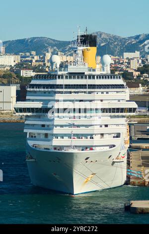 Marseille, France - 03 décembre 2024 : grand navire de croisière avec plusieurs ponts et entonnoir jaune amarré au port de Marseille. Paysage urbain et collines visibles u Banque D'Images