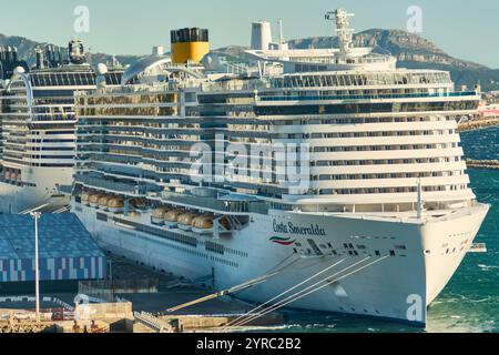 Marseille, France - 03 décembre 2024 : bateau de croisière blanc avec détails jaunes amarré au port, entouré d'installations portuaires, avec un paysage urbain et m Banque D'Images