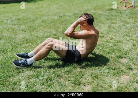 Homme en forme s'exerçant à l'extérieur effectuant des sit-ups sur un terrain herbeux Banque D'Images