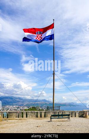 Un grand drapeau croate vole sur un haut mât sur un point de vue de la colline Marjan au-dessus de la ville de Split, ciel bleu avec des nuages blancs Banque D'Images