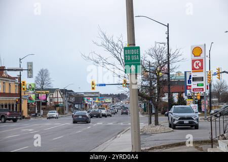 Niagara, CANADA - 21 février 2024 : scène de rue urbaine avec un panneau 'Bridge to USA', la circulation, les stations-service, et les devantures de magasins par temps couvert. Banque D'Images