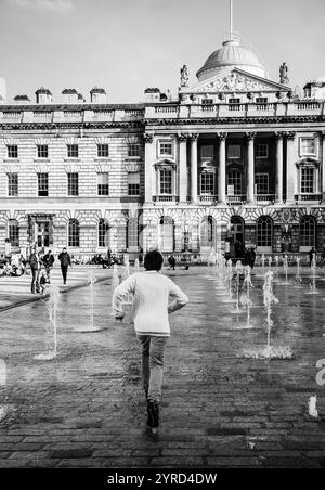 LONDRES, ANGLETERRE, Royaume-Uni - 3 MAI 2014 : garçon courant à travers les jets d'eau de la fontaine dansante dans la cour Somerset House. Photo historique noir et blanc. Banque D'Images