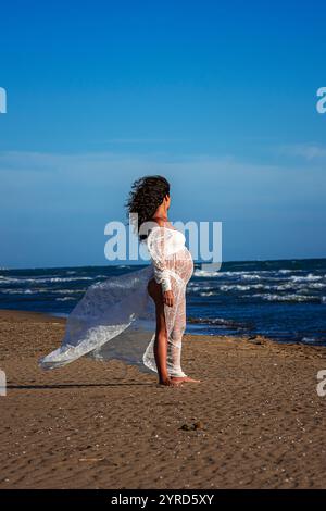 belle femme méditerranéenne aux cheveux bouclés enceinte pose sur la plage Banque D'Images