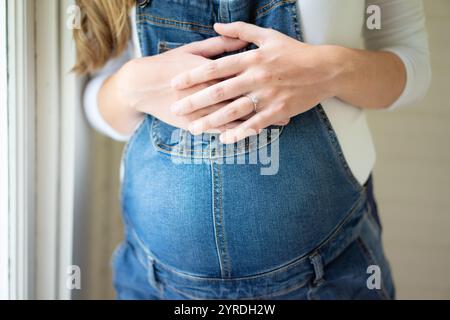 Gros plan des mains d'une femme enceinte sur le ventre dans des combinaisons denim Banque D'Images