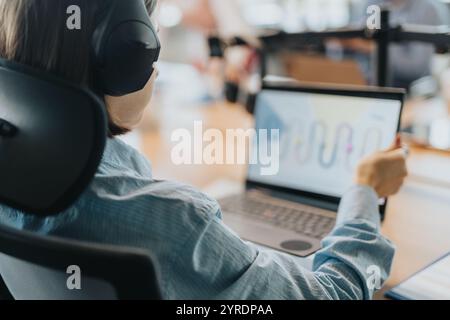 Un professionnel des affaires est assis dans une salle de réunion, portant des écouteurs, tout en analysant les données sur un ordinateur portable Banque D'Images