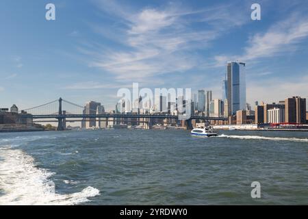 Découvrez les gratte-ciel de New York depuis le ferry par une journée ensoleillée. Les gratte-ciel s'élèvent majestueusement, le pont de Manhattan vole sur l'eau Banque D'Images