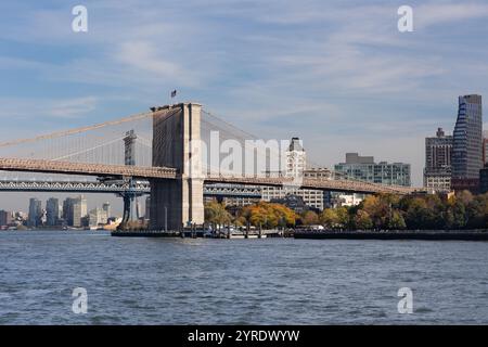 Le pont Landmark se dresse bien en vue contre un ciel dégagé, reliant Manhattan et Brooklyn. Les arbres avec des feuilles d'automne bordent le bord de l'eau Banque D'Images