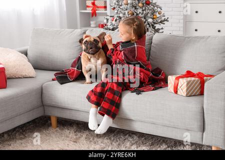 Mignonne petite fille avec bouledogue français et livre de lecture de cadeau de Noël sur le canapé à la maison Banque D'Images