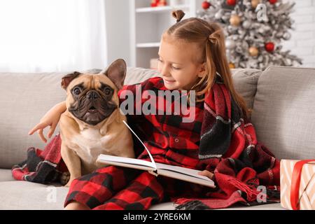 Mignonne petite fille avec bouledogue français et livre de lecture de couverture chaude sur le canapé à la maison Banque D'Images