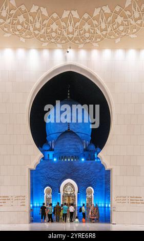 Les dômes illuminés de la Grande Mosquée Sheikh Zayed vus à travers une arche ornée la nuit, mettant en valeur l'élégance architecturale et l'ambiance spirituelle. Banque D'Images