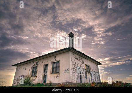 Maison blanche abandonnée, couverte de graffitis, se dresse sur fond d'un ciel dynamique et nuageux, évoquant un mélange de décomposition et de résilience Banque D'Images
