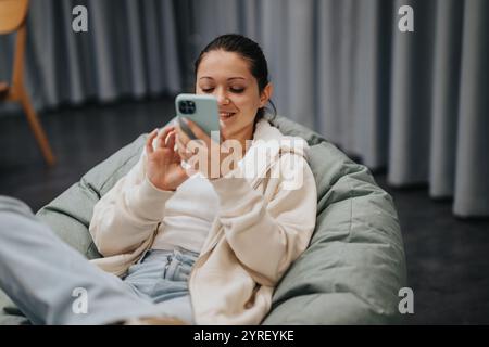 Femme détendue appréciant le temps de téléphone intelligent sur un sac de haricot confortable Banque D'Images