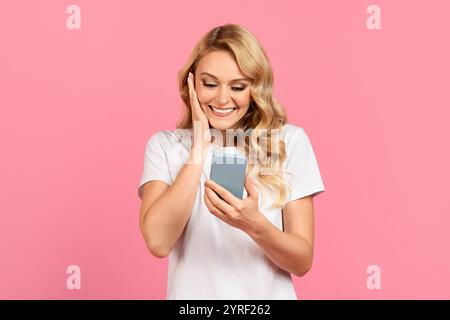 Jeune femme s'engageant heureux avec smartphone sur un fond rose Banque D'Images